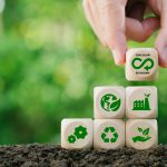 Circular economy concept.Hand holding wooden block with green bokeh background.